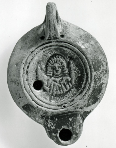 Mould-made pottery lamp with a circular body, a rounded shoulder, and a short flat-topped semicircular nozzle set into the shoulder and defined by a lateral groove. At the rear is a pierced handle, grooved along the upper edge. The discus is surrounded by two circular grooves, the outer one pierced with an air-hole. On the discus is a draped bust of Luna with the horns of a crescent moon rising on each side of her. Across the slightly raised base is the impressed name CATILIVEST, C. Atilius Vestalis.