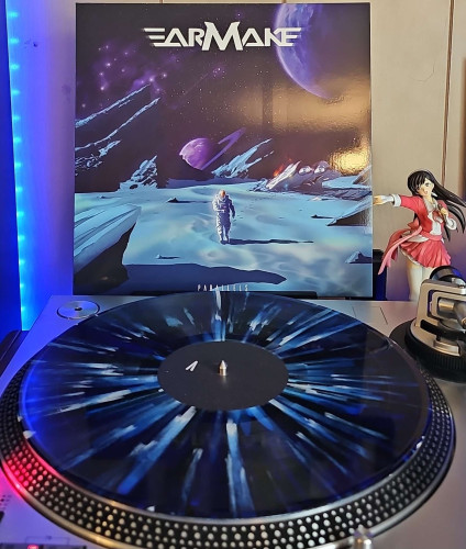 A Dark Blue Swirl w/ Light Blue and Black Splatter vinyl record sits on a turntable. Behind the turntable, a vinyl album outer sleeve is displayed. The front cover shows an astronaut walking on the surface of a lifeless planet. There are stars in the sky behind him and multiple other planets. 

To the right of the album cover is an anime figure of Yuki Morikawa singing in to a microphone and holding her arm out. 