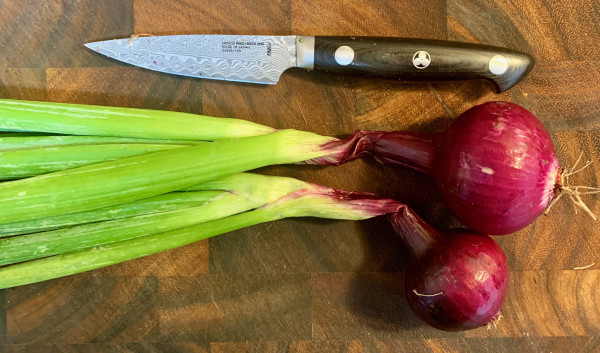 Two young red onions on a cutting board with a paring knife.