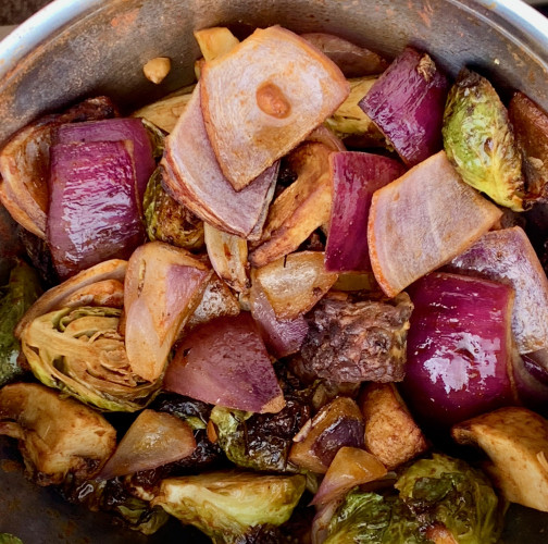 A stainless-steel bowl that contains roasted halved brussels sprouts, chunks of red onion, diced tempeh, and quarter mushrooms.