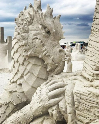 Statues of dragon and girl in sand.