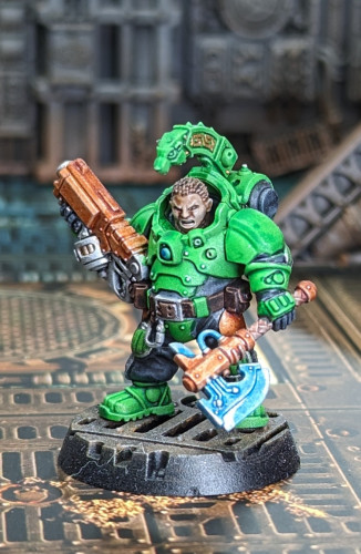Warhammer 40k Leagues if Votann Kill Team miniature painted with green armor and orange guns and lots of metallic silver bits around. The leader snarling with a gun and a glowing axe.