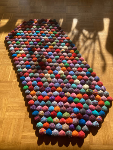 Colorful rug out of knitted hexagonal shapes lying on a wooden floor. 