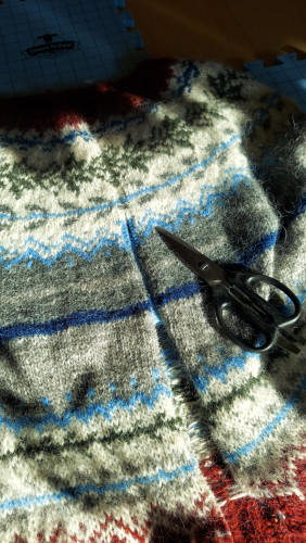 A pair of scissors laying in a partially cut steek line in a stranded colorwork knitted sweater.