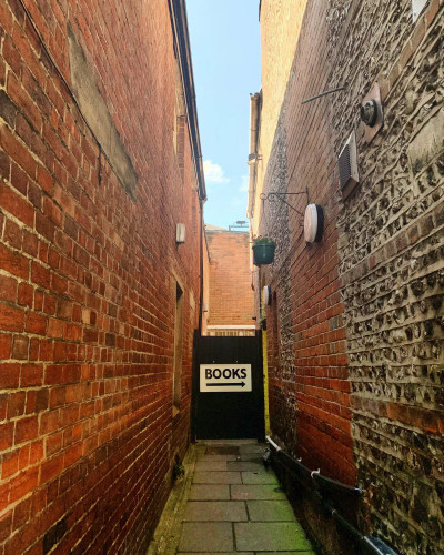 A very narrow alley with brick walls on both sides. At the end, a door with an arrow pointing to the side an the label "books"

Found by Victoria James in Winchester