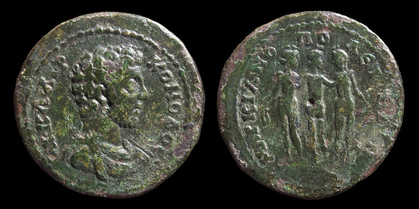 Ancient bronze coin against black background, with brittle, loden green, patina. To left, the obverse, showing a bust of the emperor Commodus and to the right, the reverse, three naked female figures, two facing forwards, the middle one facing away and with arms outstretched to the others