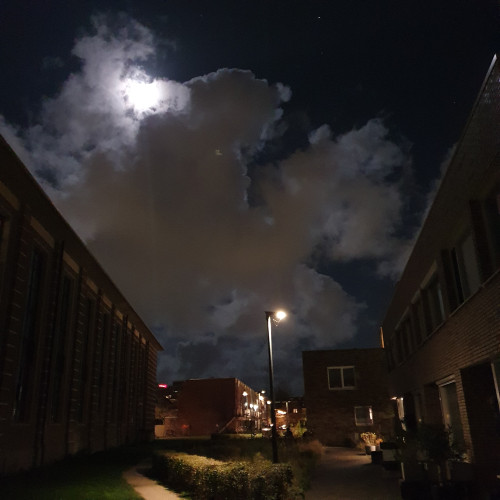 The night sky between Dutch houses with big fluffy clouds spectacularly illuminated by the almost full moon. 