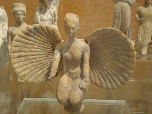 Aphrodite is kneeling, a sea shell wide open behind her back like a set of wings. Her right hand is missing but her left holds the remains of a libation bowl.