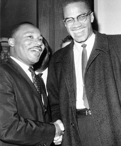 Black-and-white image of the Reverend Dr. Martin Luther King Jr. and Malcolm, X, shaking hands and smiling.