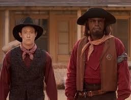 Data and Worf in cowboy outfit behind a Wild West backdrop 