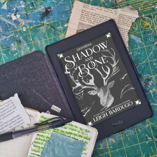 Kindle open on a green cutting mat, the Shadow and Bone book cover on the screen.