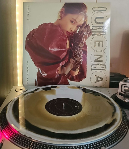 Image shows a turntable with a Gold, Black & White Swirl vinyl record on the platter. Behind the turntable vinyl album outer sleeve is displayed. The front cover shows Chung Ha in a puffy dress, looking at the camera as she leans her head on her hands