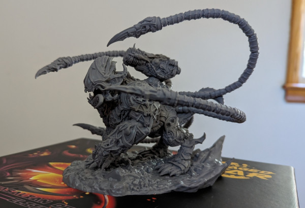 A Warhammer 40k style mini of a armored demon monster with long tentacles and a big laser cannon on is back.