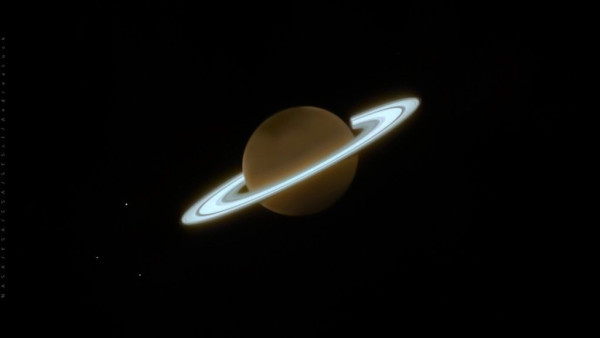 Saturn shown as a darker world with vibrant, pale blue rings. Three moons are spots of light to the left of the gas giant planet: (top) Dione, (middle) Enceladus, (bottom) Tethys.