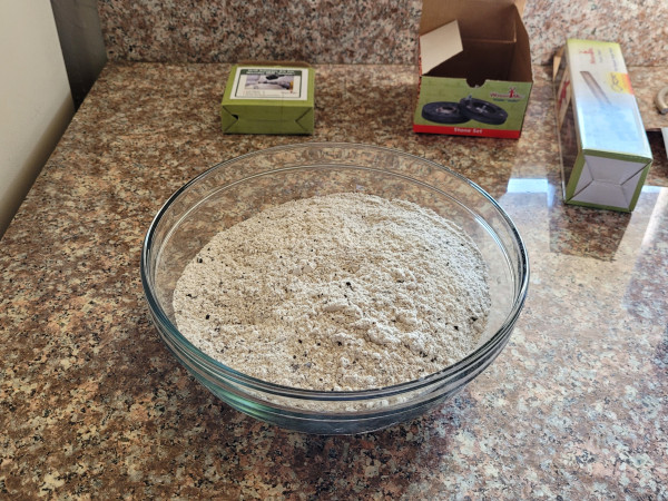 Homemade fine black bean flour sits in a fairly large mixing bowl on a kitchen counter. The flour is greyish with black flecks.