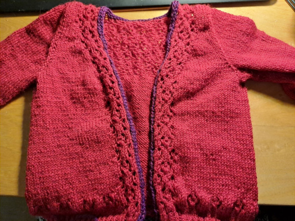 Knitted children cardigan in deep red with some lace parts, with purple edge