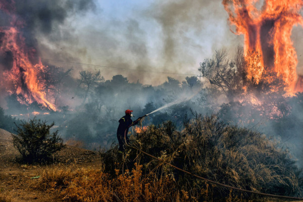 Photo of a fireman dousing flames on a wildfire at Panorama settlement near Agioi Theodori, some 70 kms west of Athens.