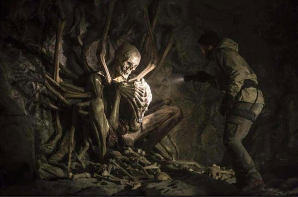 A man is in a cave shining a flashlight on an effigy made of bones.