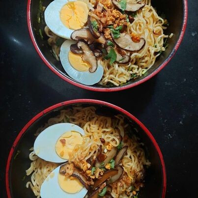 Two red-rimmed bowls of noodles on a black countertop