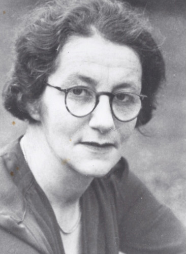 black and white head shot photo of Lois Suckling, dark hair pulled back from face, round tortoise shell glasses, slight smile looking direct at camera