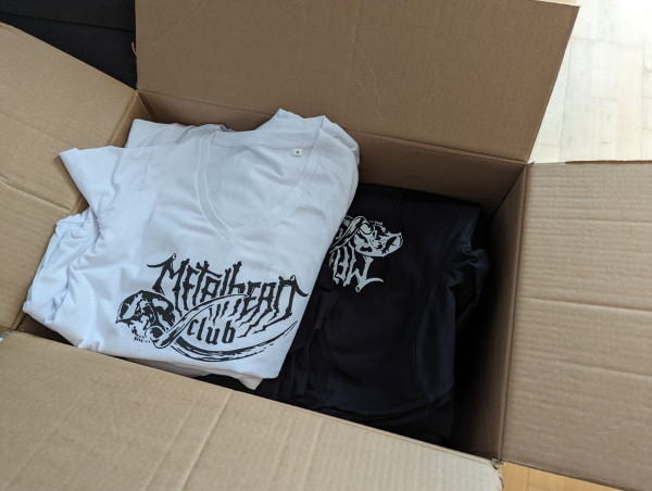 Open box with metalhead.club t-shirts in it. A black stack and a white one.