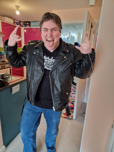 Me wearing a black leather biker jacket, my new Metalhead Club t-shirt, and blue jeans. I'm pulling a silly face and giving the sign of the horns. 🤘