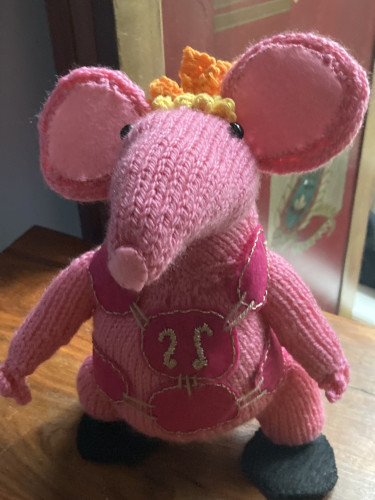 A hand knitted Clanger in pink wool, wearing a pink felt tabard
