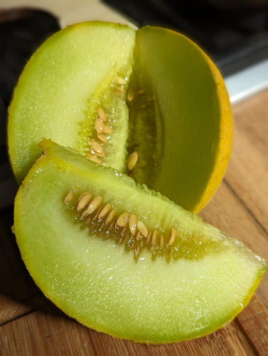 A melon that's been cut open showing the soft juicy greeny yellowy flesh and the yellow seeds