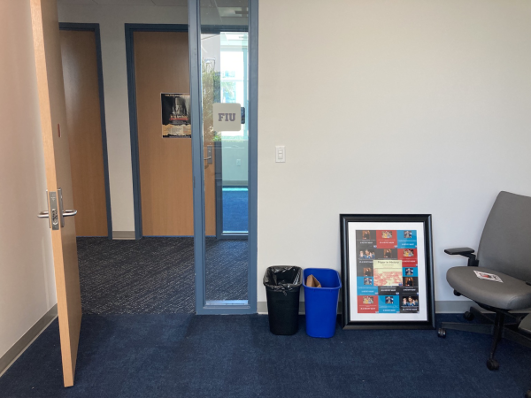 Photo from inside an empty office with one office chair, one framed picture, and two trash cans. 