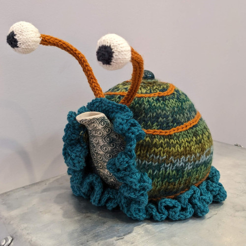 A tea cosy in yne shape pf a nsil with knittted googly eyes on long stalks