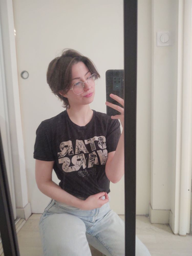 Mirror selfie of Poki wearing blue jeans and a cropped black tee with STAR WARS printed in beige on int. You can see several Star Wars characters drawn in the text