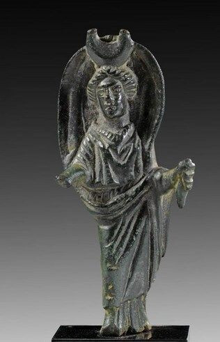 Bronze figurine of Selene with her typical iconography: a lunar crescent on her head, remnants of a torch in her left hand and a billowing cloak above her head. The right hand has broken off, it possibly used to hold a riding crop.