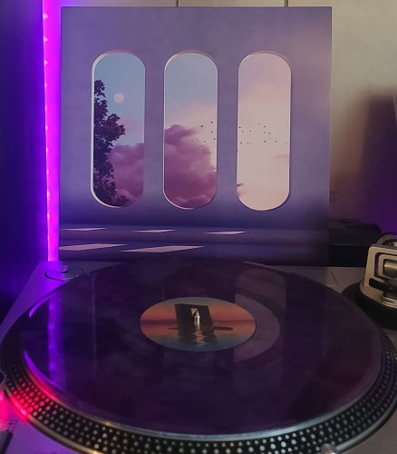 A purple marbled vinyl record sits on a turntable. Behind the turntable, a vinyl album outer sleeve is displayed. The front cover shows Steps leading up to 3 open, oblong windows. Outside you can see a tree, clouds, birds flying, and the moon. 