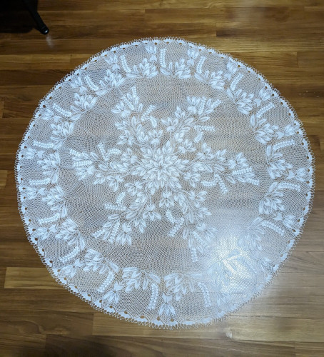 A large handknit white lace doily, with a floral and leaf motif.