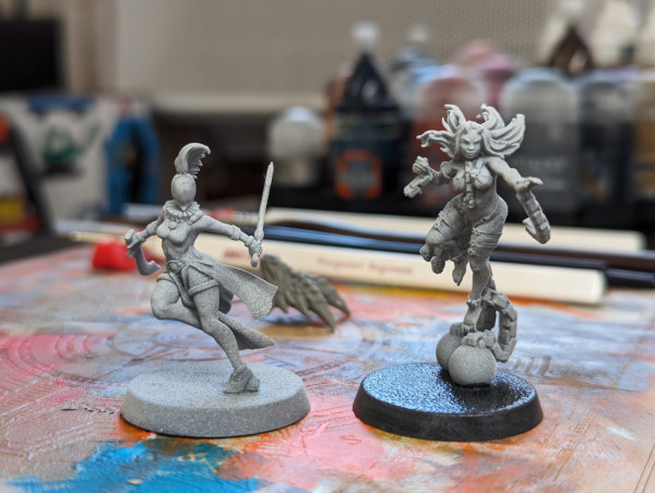 Two unpaid Warhammer 40k miniatures. A harlequin Shadowseer and a daemon possessed who had broken free of her chains. Right now they are just printed white but I hope to make them very colorful!