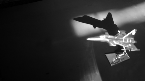 A black and white photography of a jet fighter plane of the IAS. It's a memento and is placed in a table. The shadow from the window falls on the table. It's silver in color. 