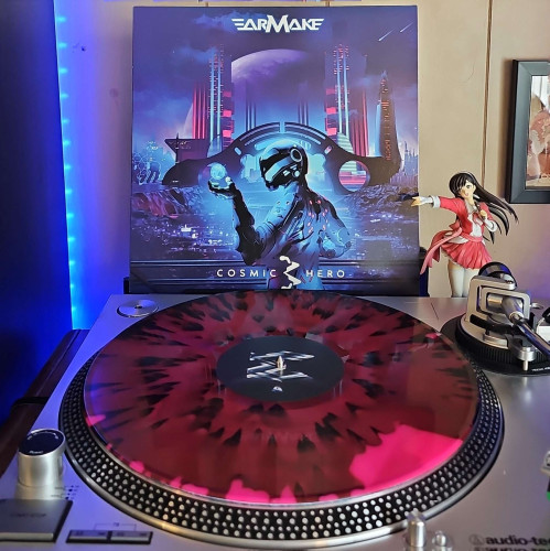 A Red, Black & Pink Swirl w/ Black & Pink Splatter vinyl record sits on a turntable. Behind the turntable, a vinyl album outer sleeve is displayed. The front cover shows a person in a futuristic suit standing in front of a futuristic city. 

To the right of the album cover is an anime figure of Yuki Morikawa singing in to a microphone and holding her arm out.
