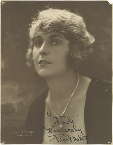 A black and white photograph of Pearl White. She has short light colored hair that is curled, and she looks wistfully up and to the viewer's left.  She wears a black dress and a pearl necklace.