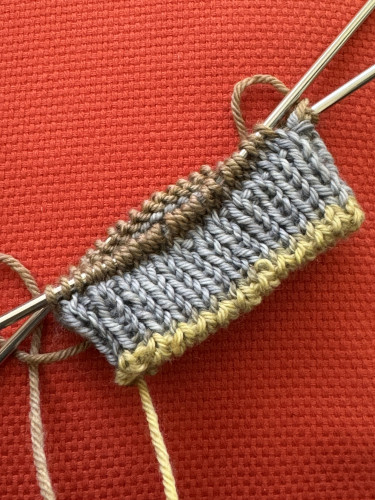 Circular knitting with tubular cast on in light green, 1x1 ribbing in pale blue, brown stitches on needle