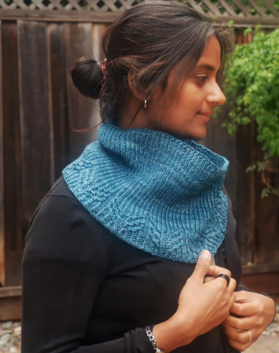 A blue cowl with twisted stitch "wings" at the bottom and ribbing for the length of the cowl