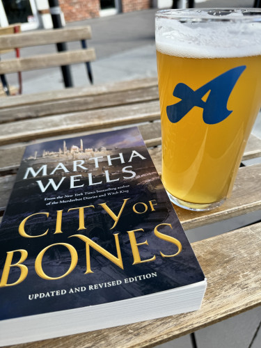 A book and a pint of beer on outside patio table. The book is: 

MARTHA WELLS
From the New York Times bestselling author
of the Murderbor Diaries and Witch King
CITY OF BONES
UPDATED AND REVISED EDITION