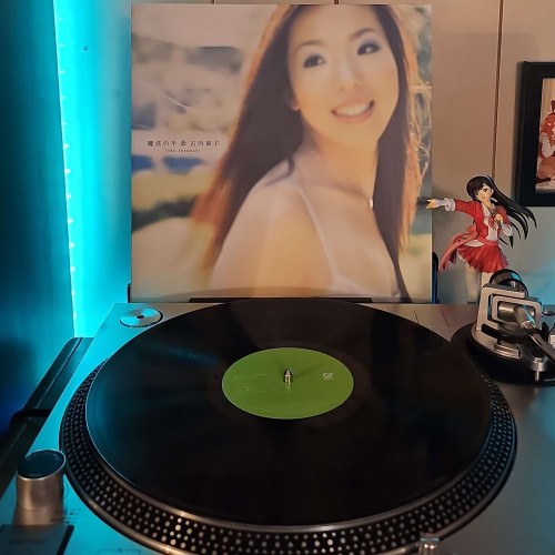 A black vinyl record sits on a turntable. Behind the turntable, a vinyl album outer sleeve is displayed. The front cover shows Toko Furuuchi looking back and smiling. 