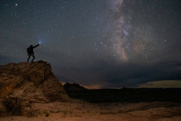 someone holds a flashlight pointing out at the milky way peeking through the clouds. 
