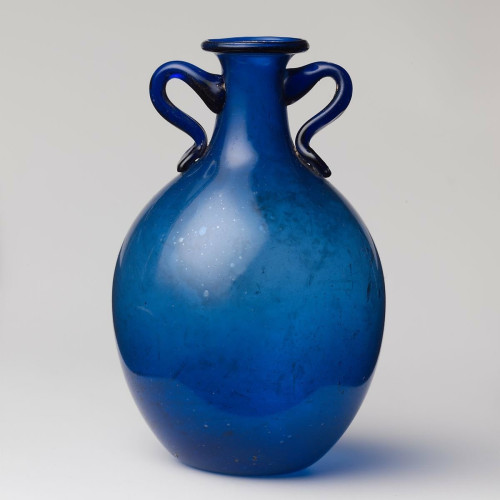 Description from the museum: ‘Translucent cobalt blue; handles in same color.
Everted rim, folded down, round, and in; flaring mouth; cylindrical neck, expanding downwards; ovoid body; concave bottom; two rod handles applied to side of neck, drawn up, round, down, and in in a curving loop, and pressed on to base of neck and top of body with flat pad and sliced off edge.
Intact; many bubbles, with a few very large; little weathering on exterior, patches of faint weathering and iridescence on interior.’