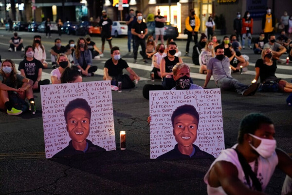 Photograph of one of the many protests that took place in Denver and Aurora Colorado following Elijah's death.  The street is lined with people sitting and standing with two individuals in the foreground holding posters with artist renderings of Elijah also showing his last words:

""I can't breathe. I have my ID right here. My name is Elijah McClain. That's my house. I was just going home. I'm an introvert. I'm just different. That's all. I'm so sorry. I have no gun. I don't do that stuff. I don't do any fighting. Why are you attacking me? I don't even kill flies! I don't eat meat! But I don't judge people, I don't judge people who do eat meat. Forgive me. All I was trying to do was become better. I will do it. I will do anything. Sacrifice my identity, I'll do it. You all are phenomenal. You are beautiful and I love you. Try to forgive me. I'm a mood Gemini. I'm sorry. I'm so sorry. Ow, that really hurt! You are all very strong. Teamwork makes the dream work. [after vomiting] Oh, I'm sorry, I wasn't trying to do that. I just can't breathe correctly."
