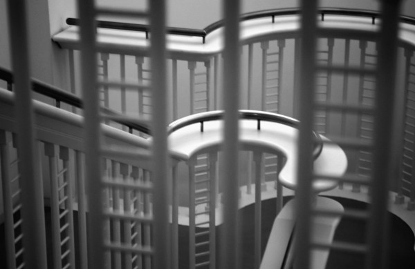 Black and white picture of a staircase landing seen through the bars of the top landing. 