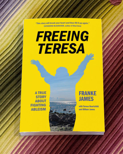 Franke James' book cover in sunny yellow for "Freeing Teresa: A True Story about Fighting Ableism." The book is sitting on a striped, multi-hued couch.