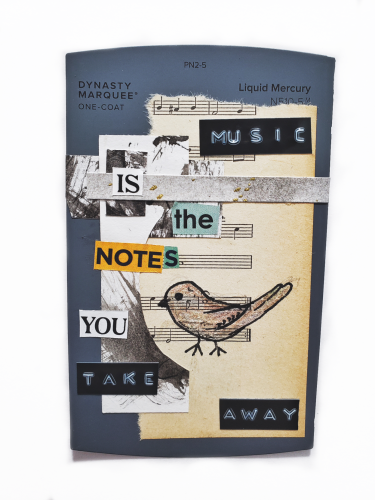 Inked pages with a piece of torn sheet music. A small bird drawn on it. Cut out words that say "music is the notes you take away"