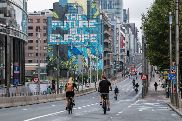 A photo of Rue de la Loi/Wetstraat in Brusells, Belgium during Car Free Sunday in Brussels on 17 September 2023.

In the photo, the people drive their bicycles on a car-free road.

A very large mural with the text "The future is Europe" stands out among the many buildings surrounding the street. 