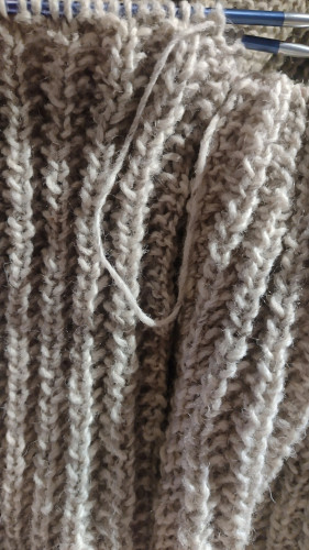 Closeup of a knitting project. Yarn is undyed, rustic. Stitch pattern is mistake rib stitch.